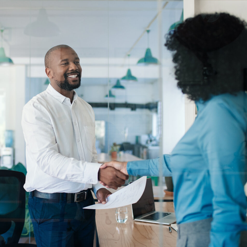 Smiling African American manager shaking hands with a new job applicant after an interview while standing together in his office